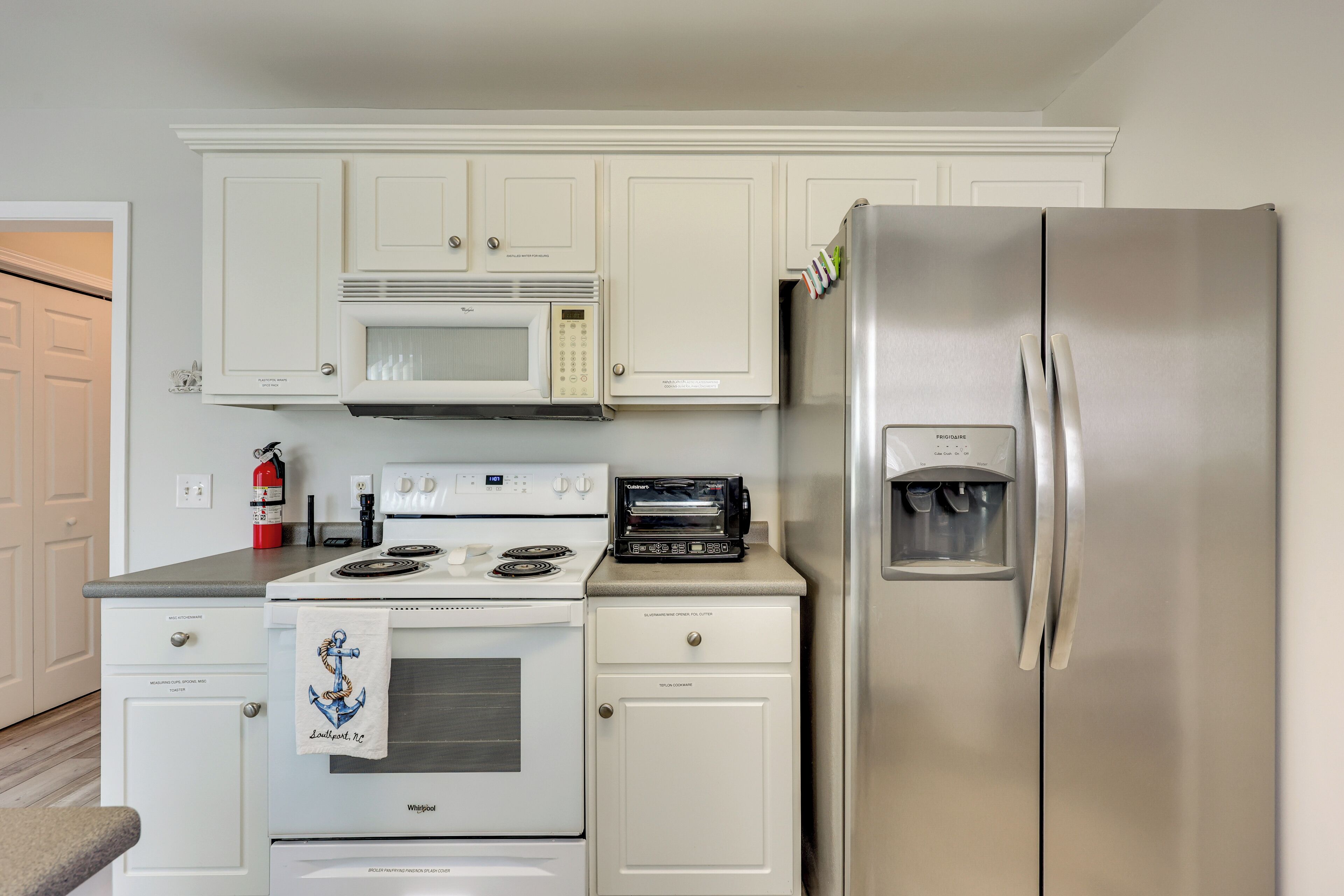 A compact kitchen with white cabinetry, a stainless steel refrigerator, a microwave, and a toaster oven.