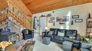 A cozy living room with a fireplace, leather sofa, and a staircase with wooden railings. - Deck & Wooded Views: 5-acre Auberry Retreat! (Auberry)