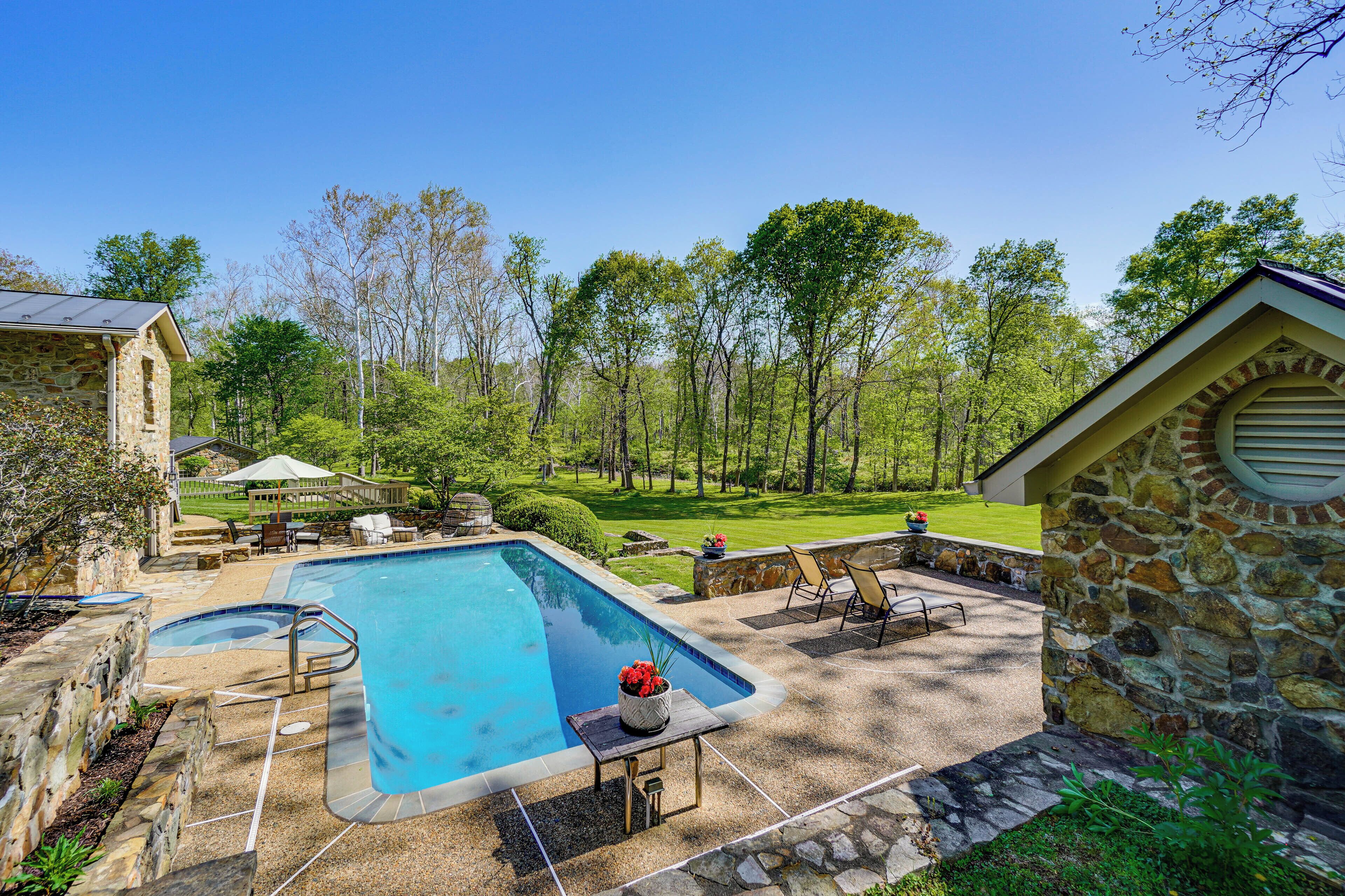 A swimming pool with a stone deck, a stone building, and a grassy yard with trees.