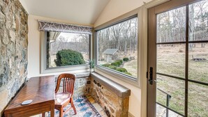 A corner room with a stone wall, a wooden table, a chair, and a large window with a view of a yard and trees. - Aldie Home w/ Private Pool: Near Wineries! (Aldie)