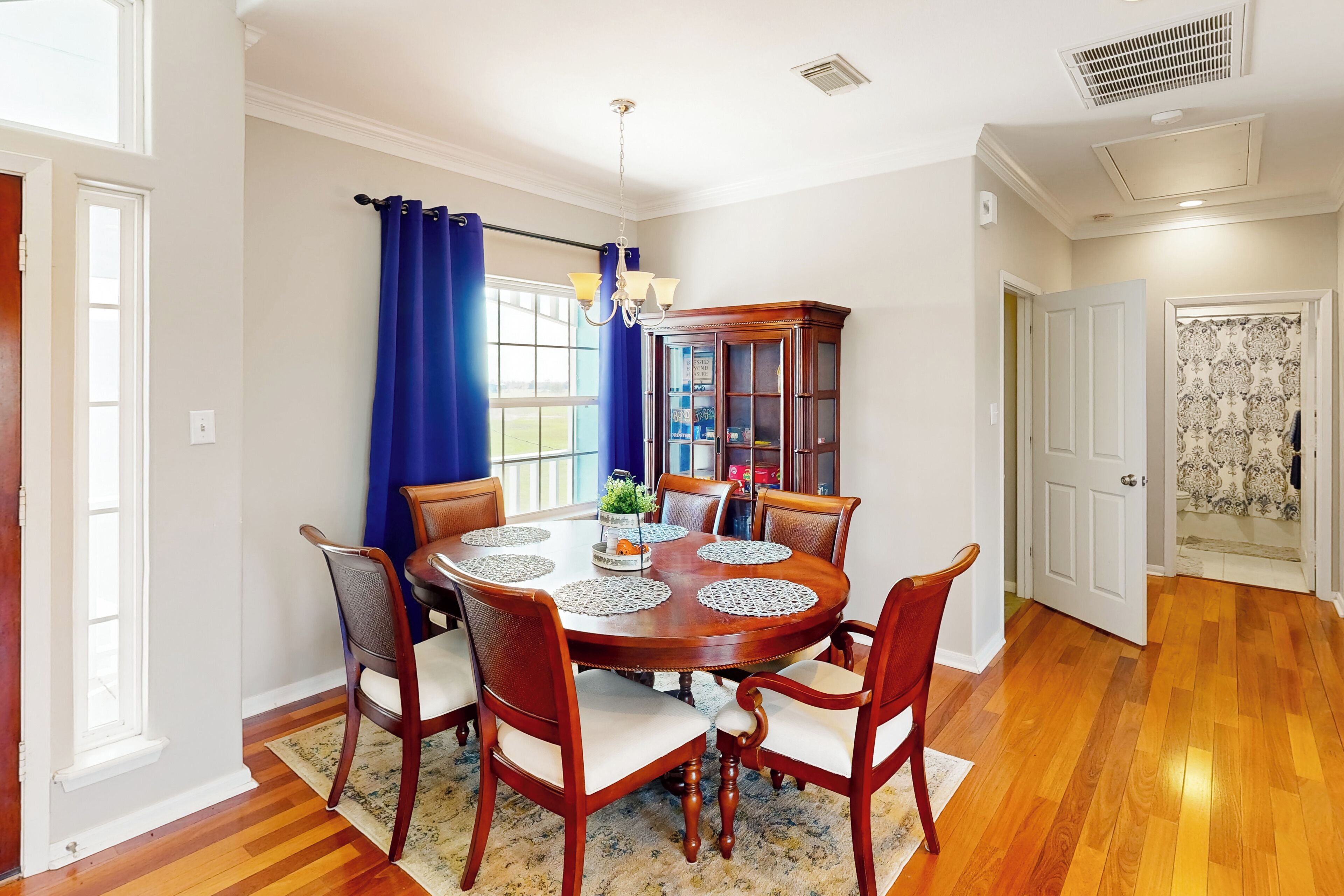 A dining room with a round wooden table, six chairs, a chandelier, and a blue curtain.
