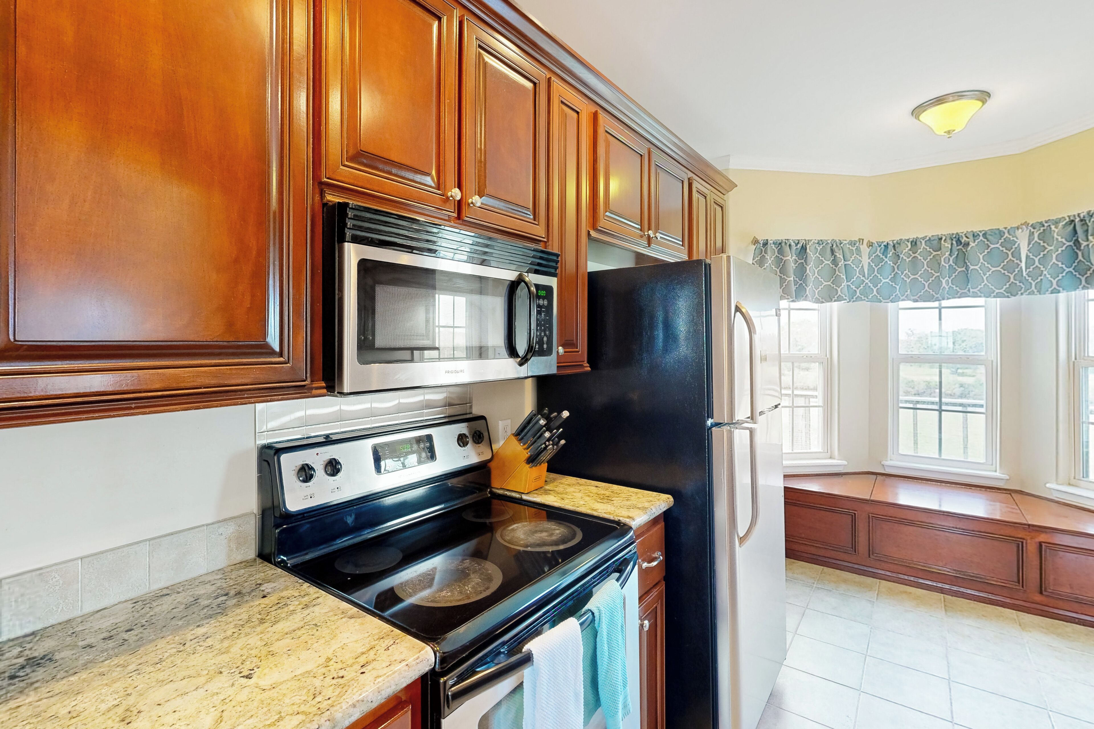 A kitchen with wooden cabinets, a stainless steel microwave, a black refrigerator, and a stove.