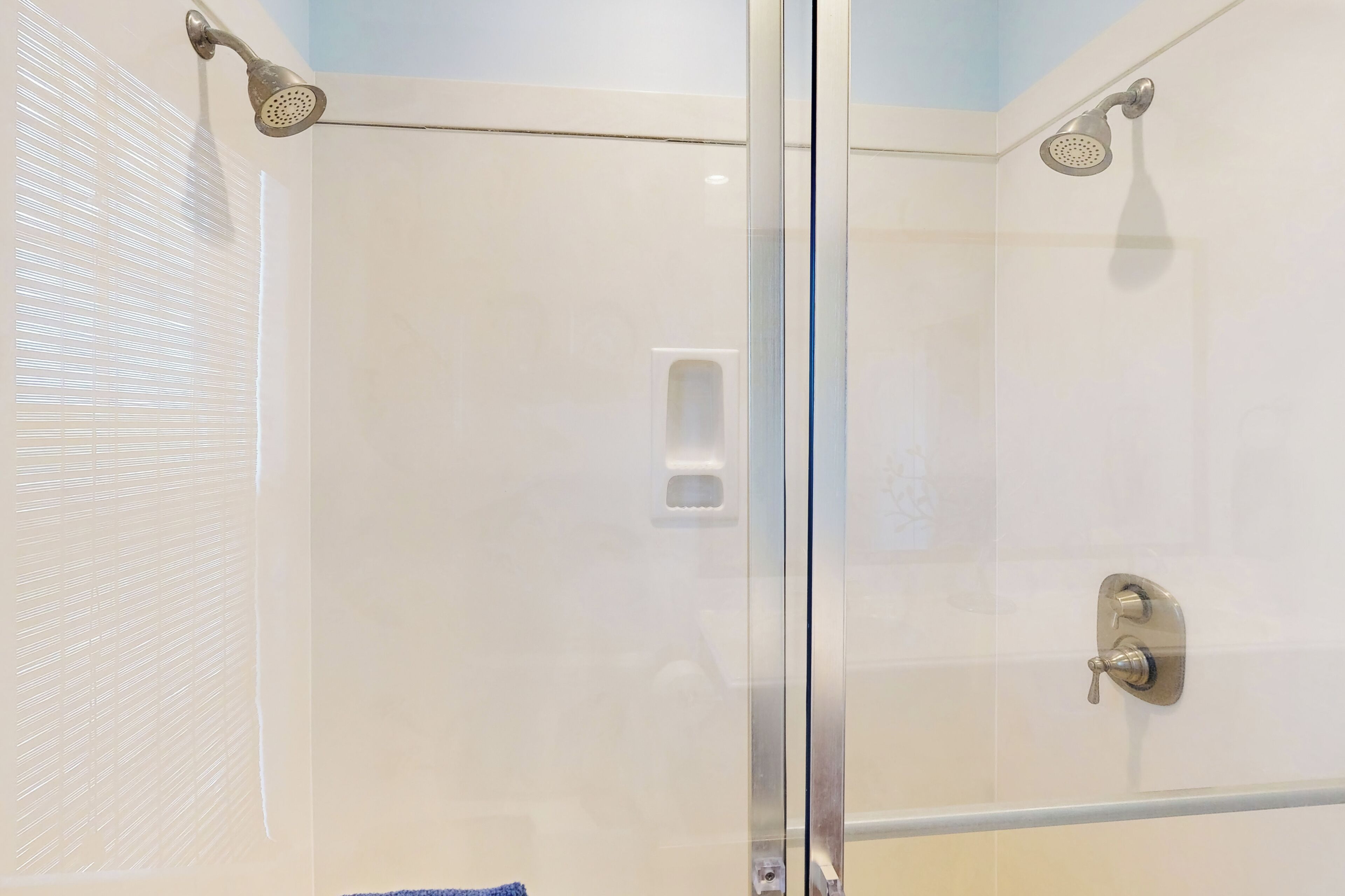 Ducha envuelta en vidrio con cabezal de ducha de mano y cabezal de ducha empotrado.