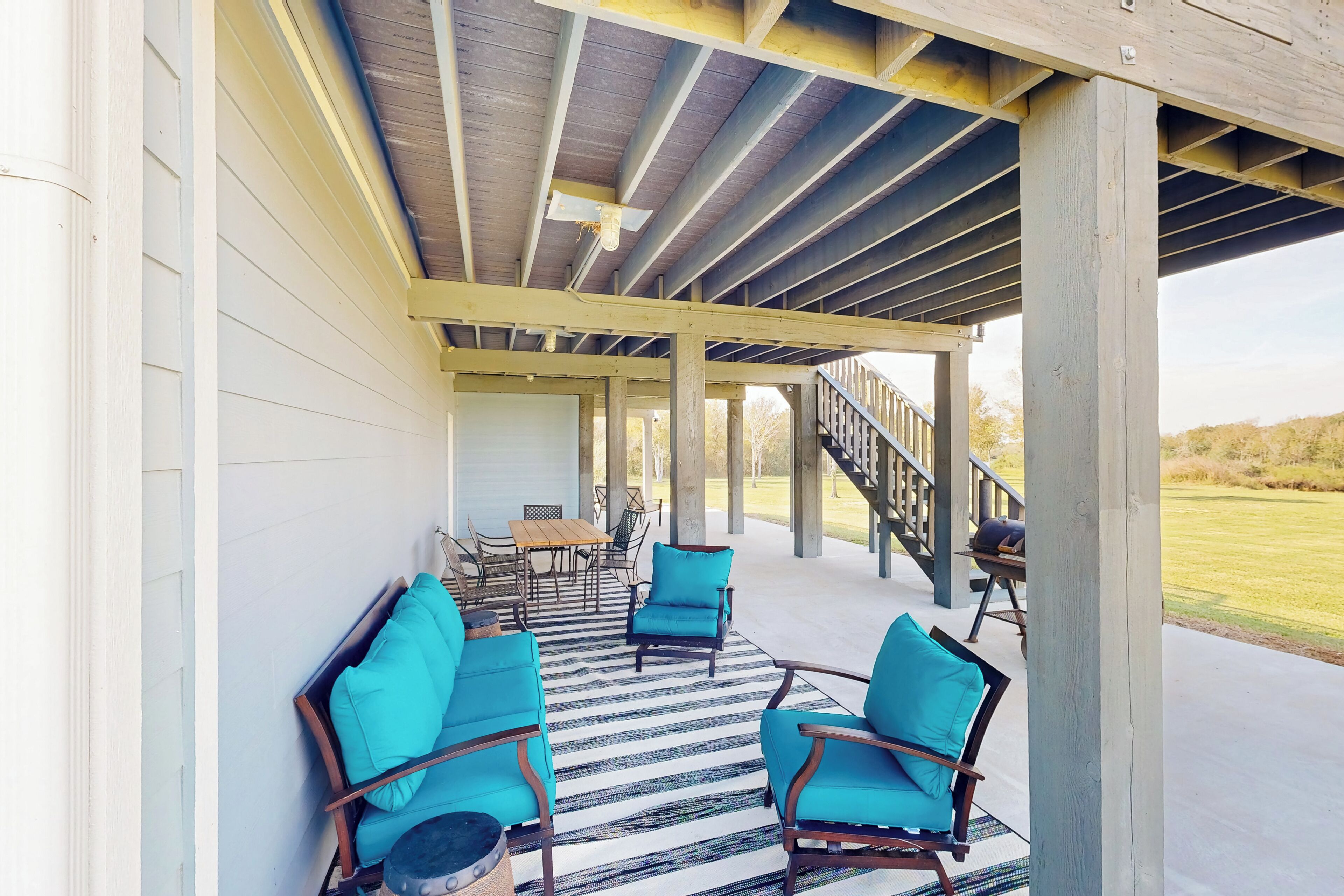 An outdoor covered patio with wooden furniture and a striped rug.