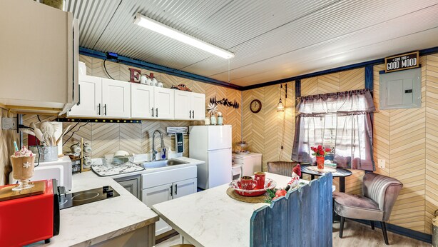 A kitchen with white cabinets, a red toaster, and a dining area with a wooden herringbone wall and a clock.