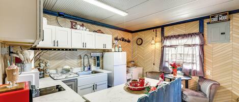 Una cocina con armarios blancos, un tostador rojo y una zona de comedor con pared de madera en espiga y un reloj.