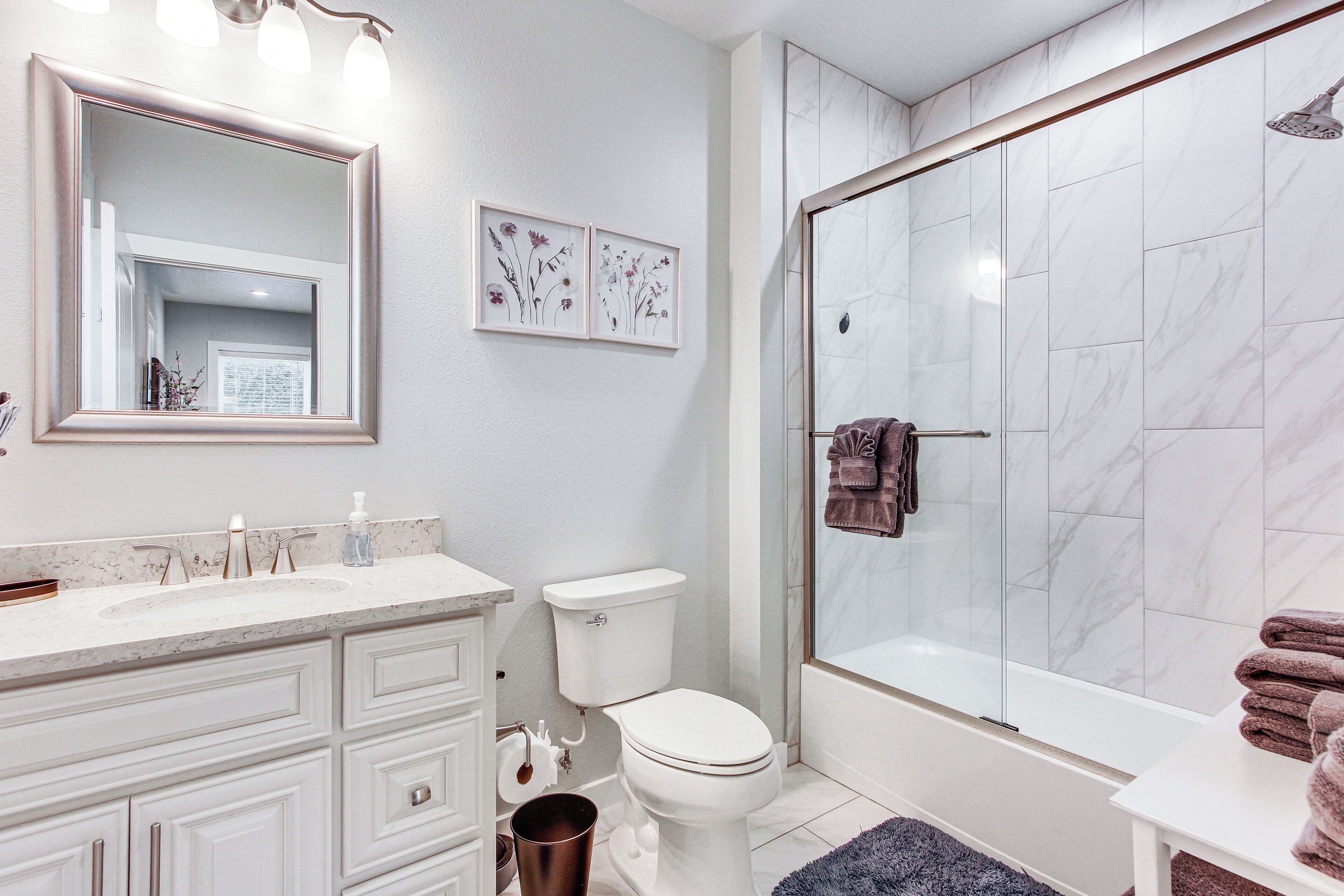 A bathroom with a white sink, toilet, and shower. There are framed floral pictures on the wall and a towel rack with towels.