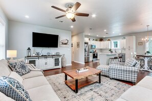 A spacious living room with a large ceiling fan, a flat-screen TV, and a dining area with a chandelier. - Steps to Sand! Family-friendly Long Beach Escape (Long Beach)