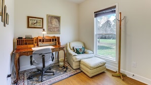 Une pièce avec un bureau en bois, une chaise rembourrée, un lampadaire et une fenêtre donnant sur une cour.