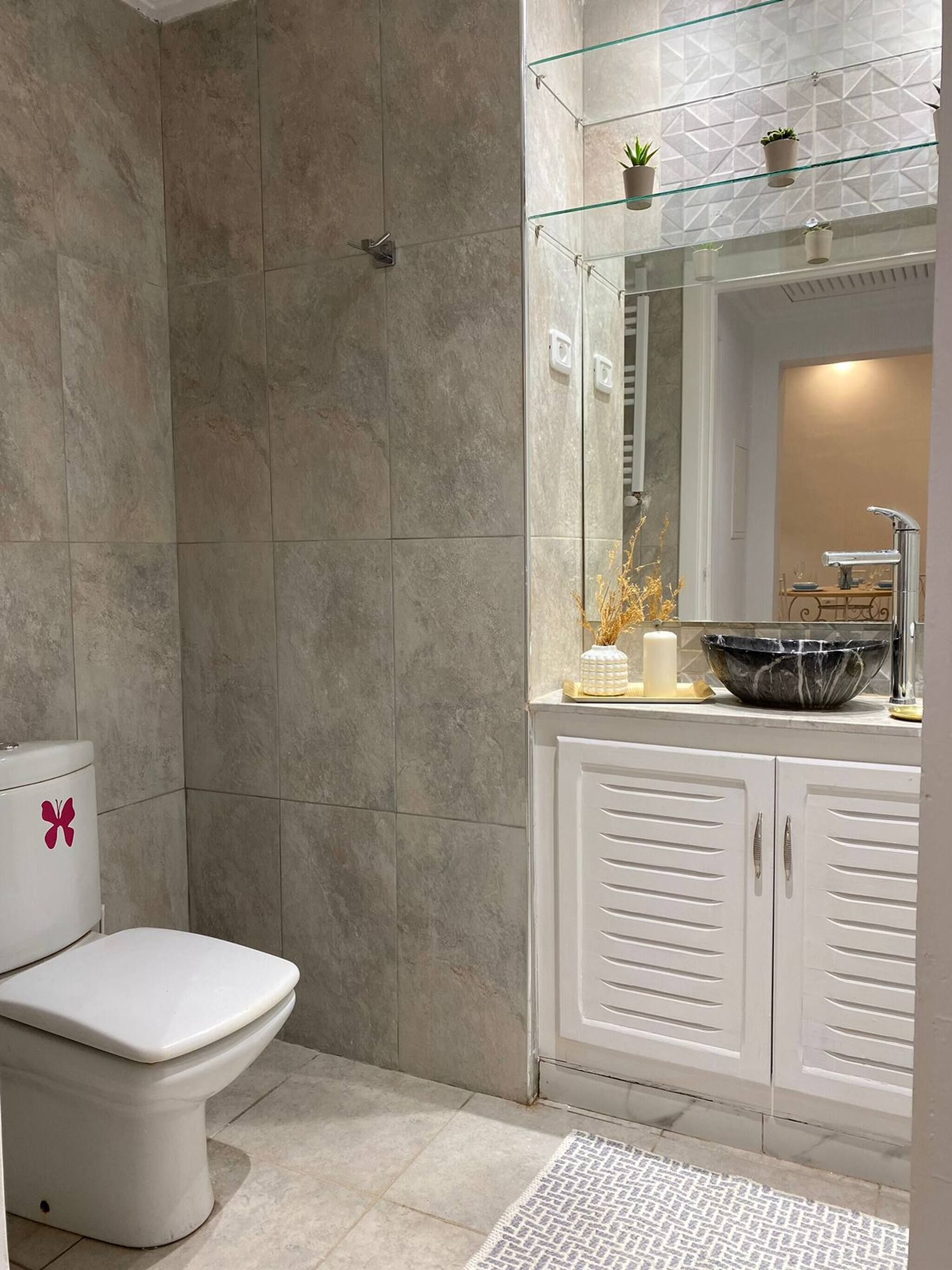A bathroom with a toilet, a glass shower enclosure, a sink with a marble basin, and a mirror above the sink.