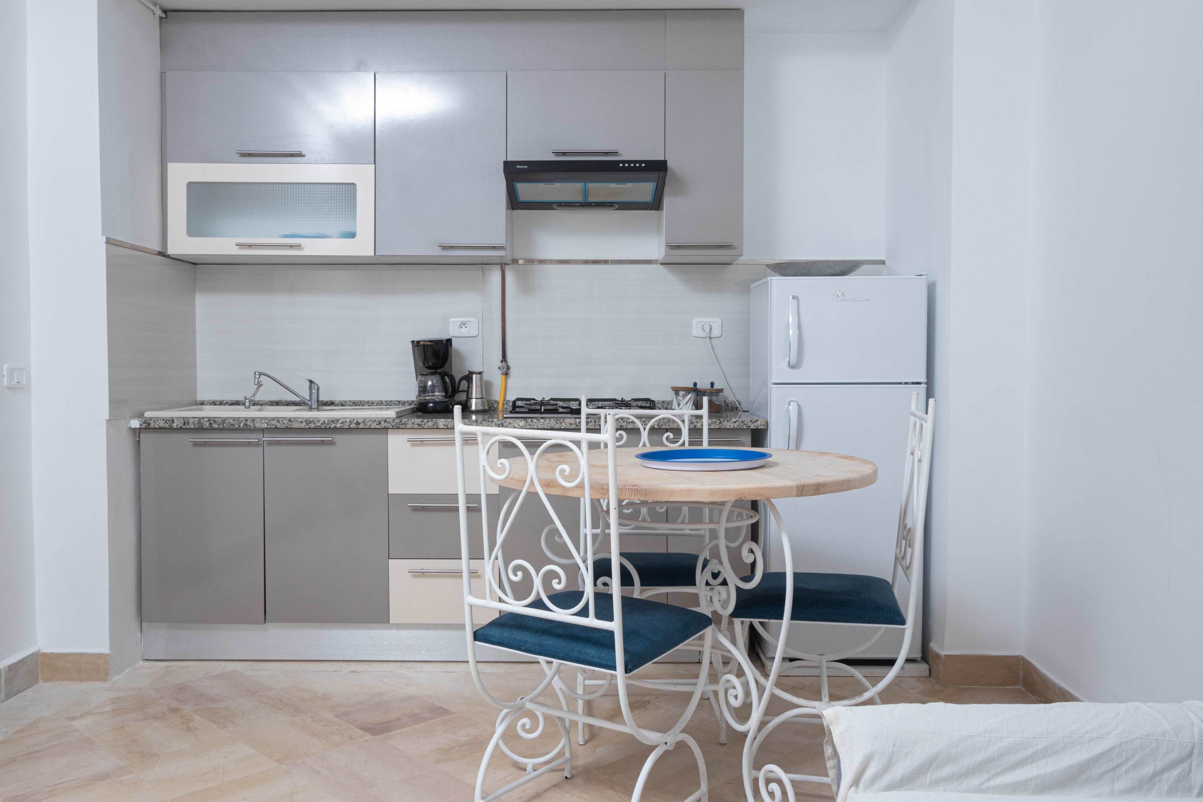 A compact kitchen with a microwave, stove, and refrigerator. There is a small dining table with a chair.