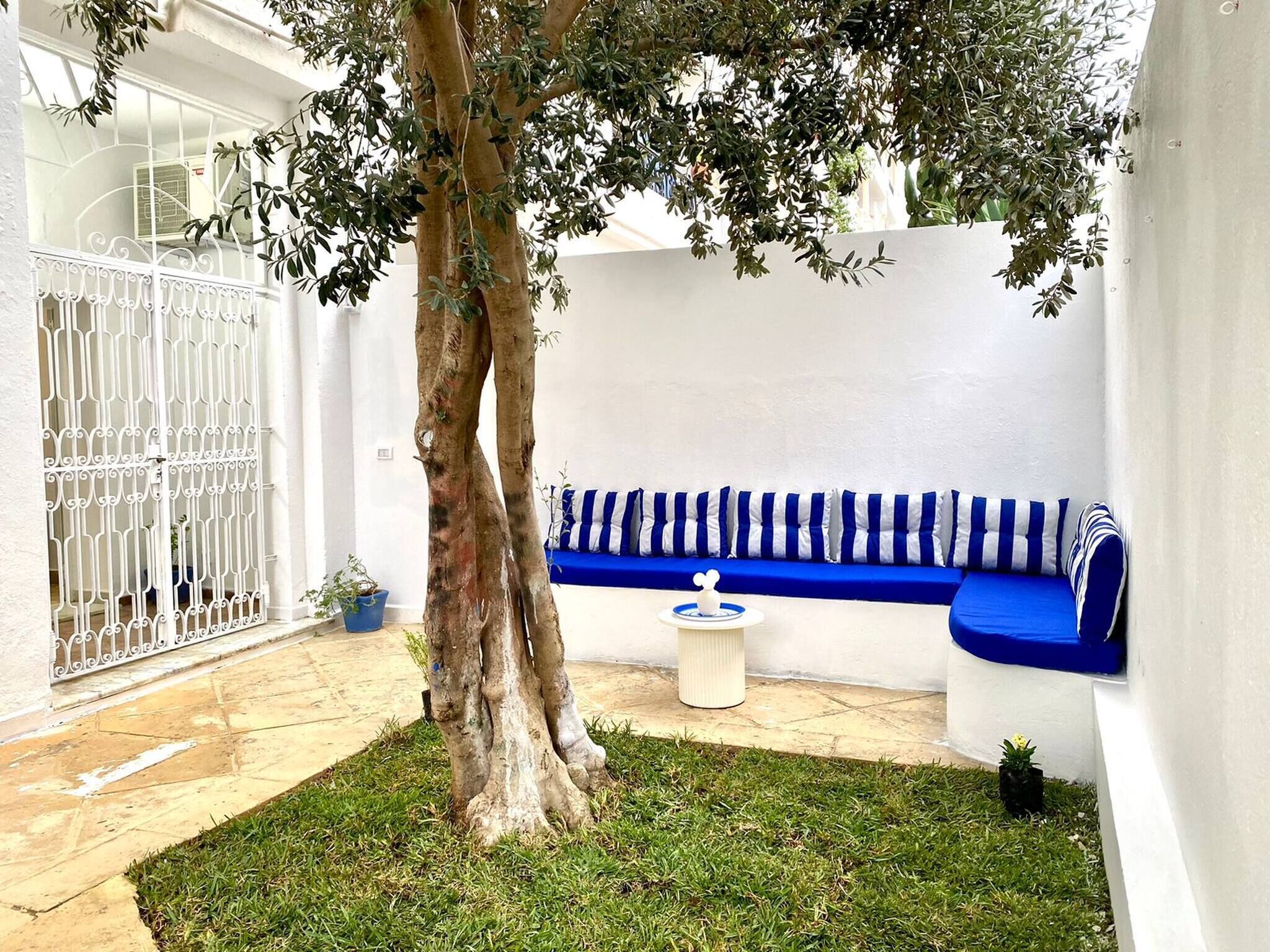 A courtyard with a tree, a blue and white striped sofa, and a white coffee table.