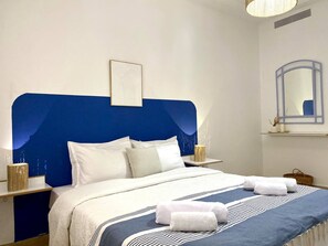 A neatly made bed with a blue headboard, white bedding, and two rolled towels on the bed. - Le Petit Zéphyr House Near the Beach (La Marsa)