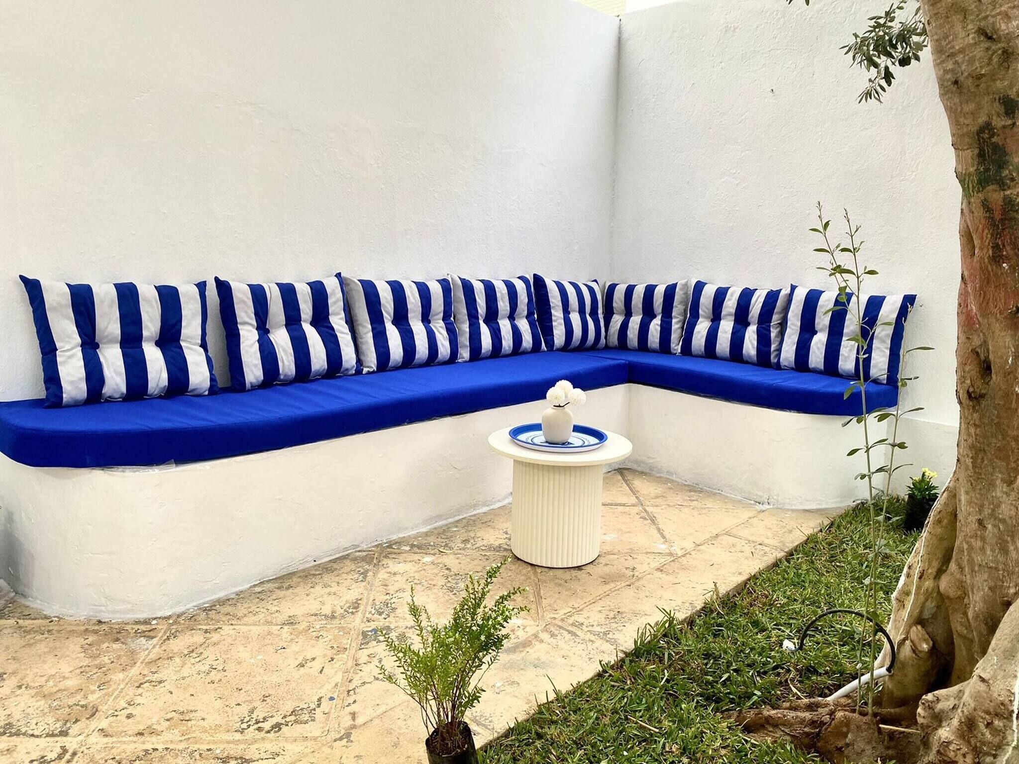 A corner seating area with a blue and white striped sofa, a small round table with a vase, and a potted plant.