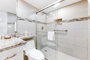 Une salle de bain moderne avec une douche à parois de verre, des toilettes blanches et un comptoir en marbre.