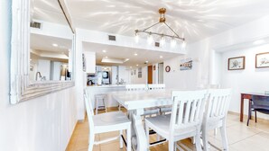 A spacious dining area with a white table and chairs, a kitchen in the background, and a ceiling light fixture. - 2BR w/ Gulf-view Balcony: Suntide III - Unit 307 (South Padre Island)