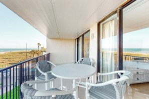 A balcony with a white table and chairs, overlooking a beach. - 2BR w/ Gulf-view Balcony: Suntide III - Unit 307 (South Padre Island)