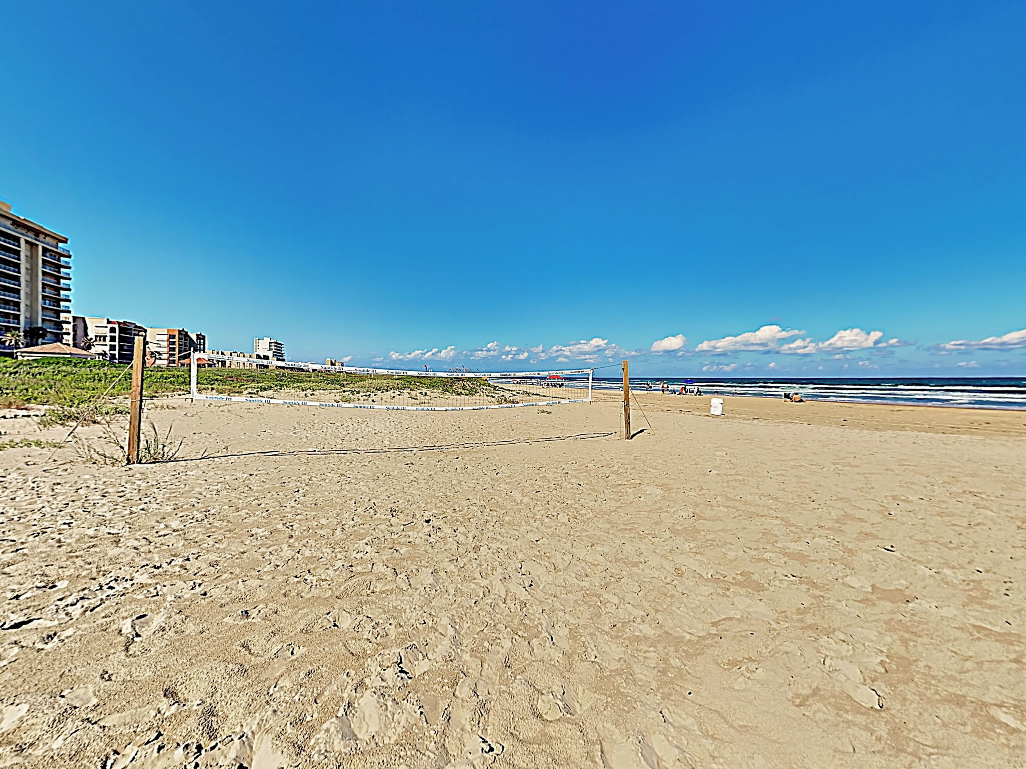Una playa con una red de voleibol, arena y edificios al fondo.