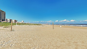 Una playa con una red de voleibol, arena y edificios al fondo.