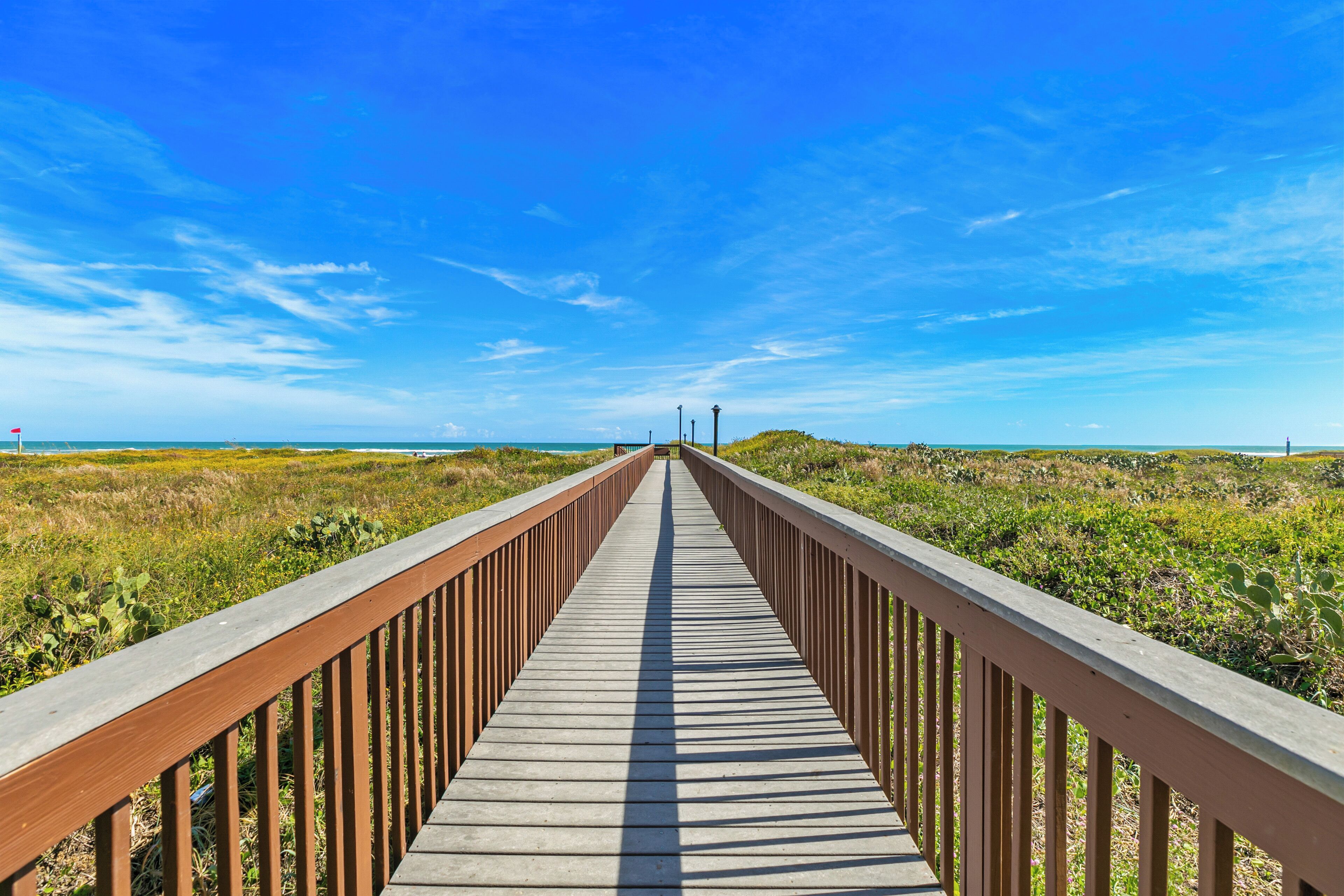 A wooden boardwalk leading to a beach with a clear blue sky.
