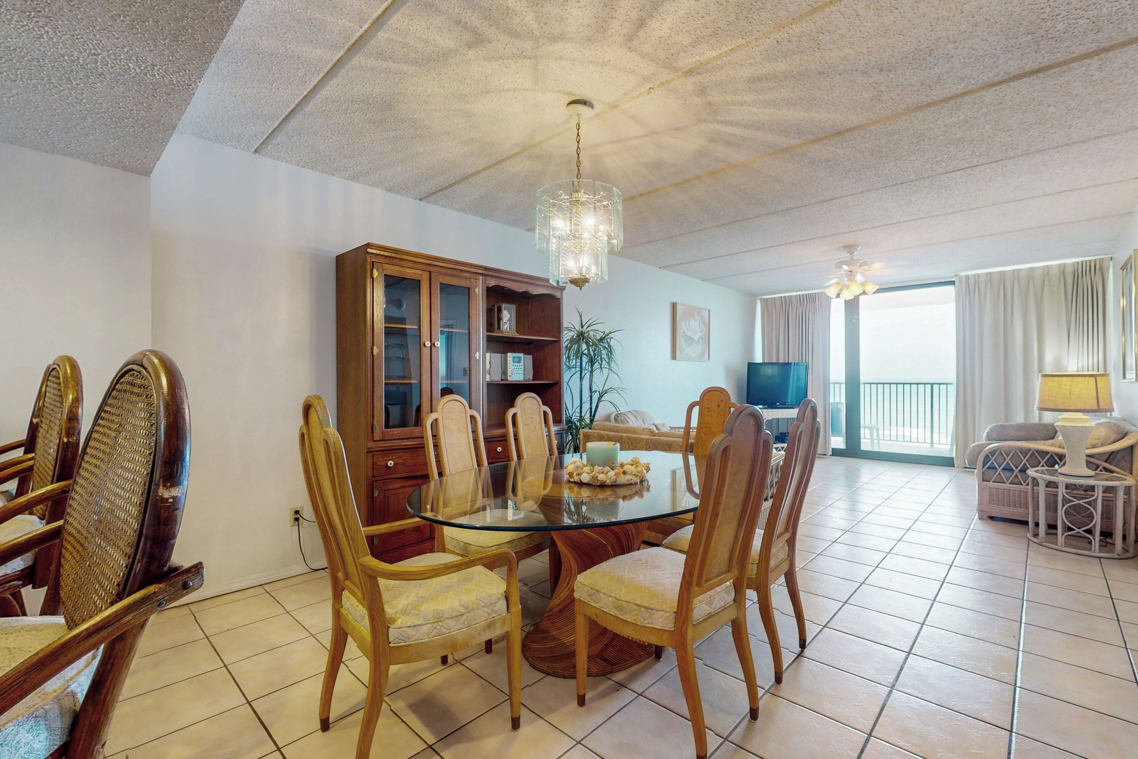 A dining area with a glass table surrounded by wooden chairs, a wooden cabinet, and a chandelier.