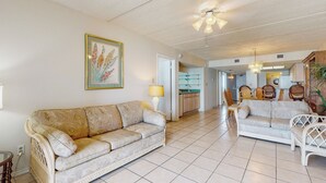 Un vaste salon avec deux canapés, un coin repas avec des chaises, une cuisine à l’arrière-plan et un ventilateur de plafond.