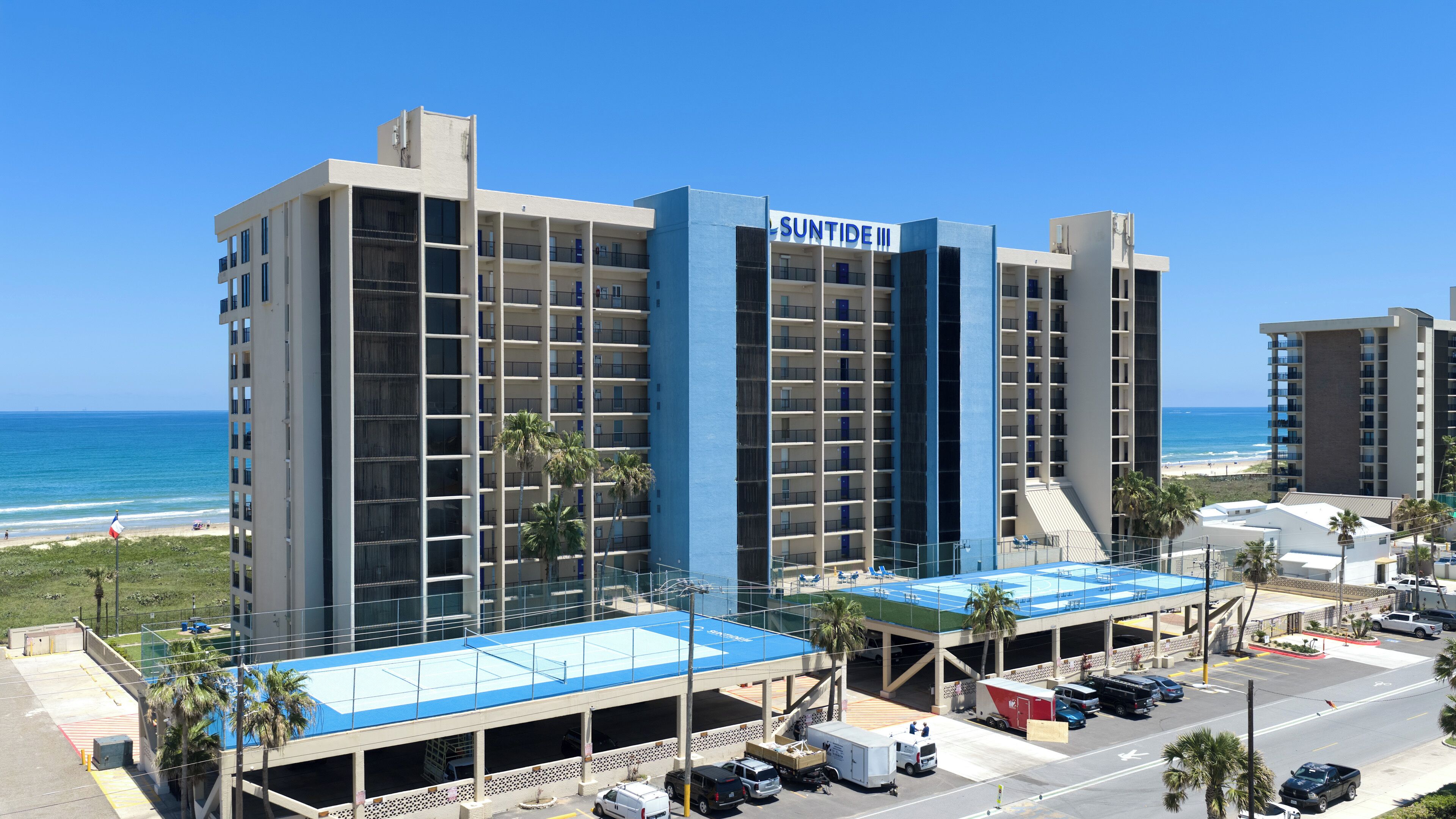 Ein mehrstöckiges Hotel mit blauer Fassade, einer Tiefgarage und Blick auf den Strand.