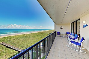 A balcony with a view of the beach, a table, and blue chairs. - 3BR Gulf-view Suite w/ Pools, Gym & Tennis (South Padre Island)