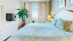 Una habitación de hotel con una cama, televisor, planta y ventana con cortinas.