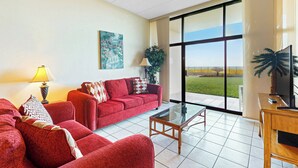 Un salón amplio con un sofá rojo, una mesa de centro de vidrio y un ventanal con vistas al exterior.