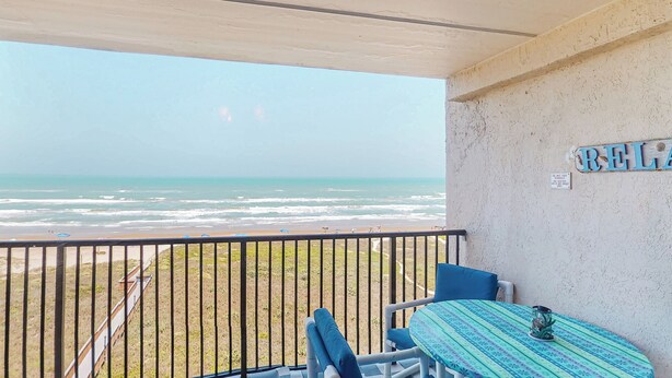Un balcón con vista a la playa, una mesa con mantel estampado y un letrero en la pared.