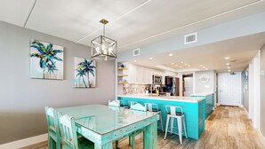 A modern kitchen with white cabinets, a central island, and a dining area with a glass table and turquoise chairs. - All-suite 2BR w/ Gulf-view: Suntide III - Unit 407 (South Padre Island)