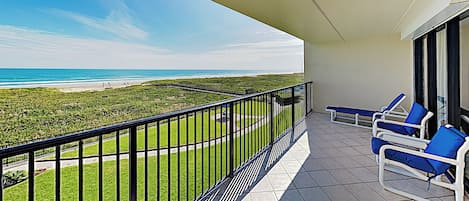 A balcony with a view of the beach, a railing, and two lounge chairs.