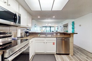 A modern kitchen with stainless steel appliances, white cabinetry, and a granite countertop. - Resort Perks & Gulf Views: Suntide III - Unit 304 (South Padre Island)