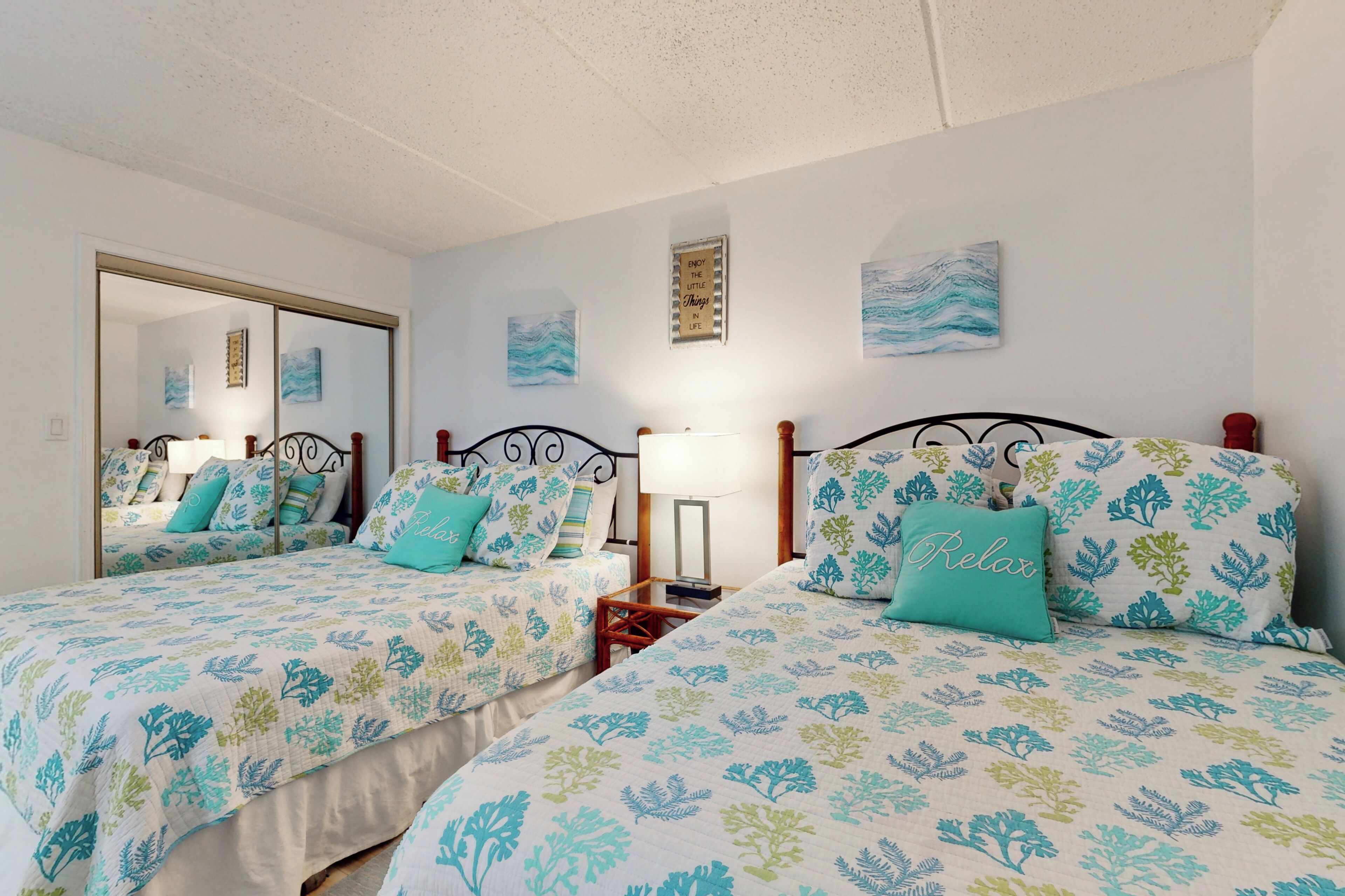 A bedroom with two beds, each with matching floral bedding and a central nightstand with a lamp.