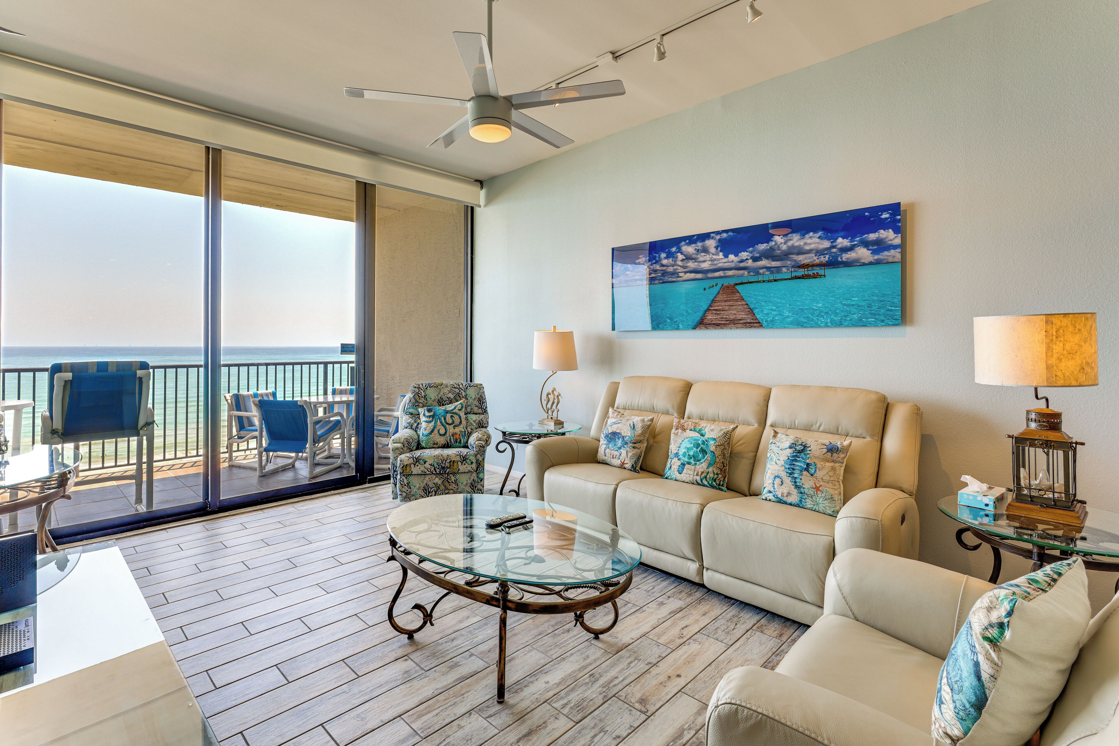 A living room with a glass coffee table, a sofa, a chair, a lamp, and a painting of a beach scene.