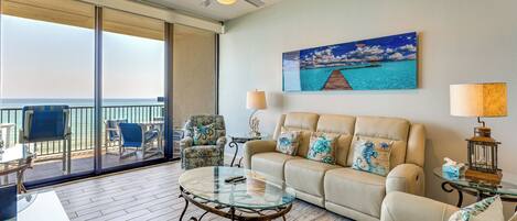 A living room with a glass coffee table, a sofa, a chair, a lamp, and a painting of a beach scene.
