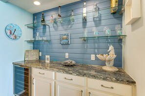A kitchen with a blue wall, glass shelves with bottles, a clock with seashells, and a decorative seahorse. - 2BR Penthouse Beach Perch: Suntide III - Unit 1207 (South Padre Island)