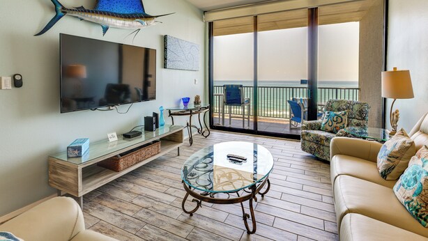 Un salon équipé d’un téléviseur, d’une table basse en verre, d’un canapé et de fauteuils, un balcon avec vue et un ventilateur de plafond.