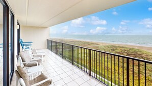 A balcony with white chairs and a table, overlooking a beach with a clear sky. - 3BR Gulf-view Resort Condo: Suntide III - Unit 605 (South Padre Island)