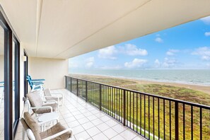 A balcony with white chairs and a table, overlooking a beach with a clear sky. - 3BR Gulf-view Resort Condo: Suntide III - Unit 605 (South Padre Island)