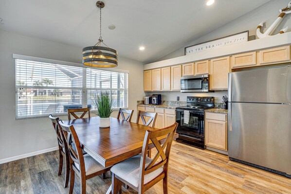 A modern kitchen with wooden cabinets, stainless steel appliances, and a dining area with a wooden table and chairs. - Boat Dock & Lanai: Waterfront Oasis in Cape Coral! (Cape Coral)