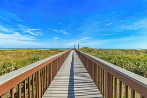 Ein hölzerner Steg führt zu einem Strand unter blauem Himmel.
