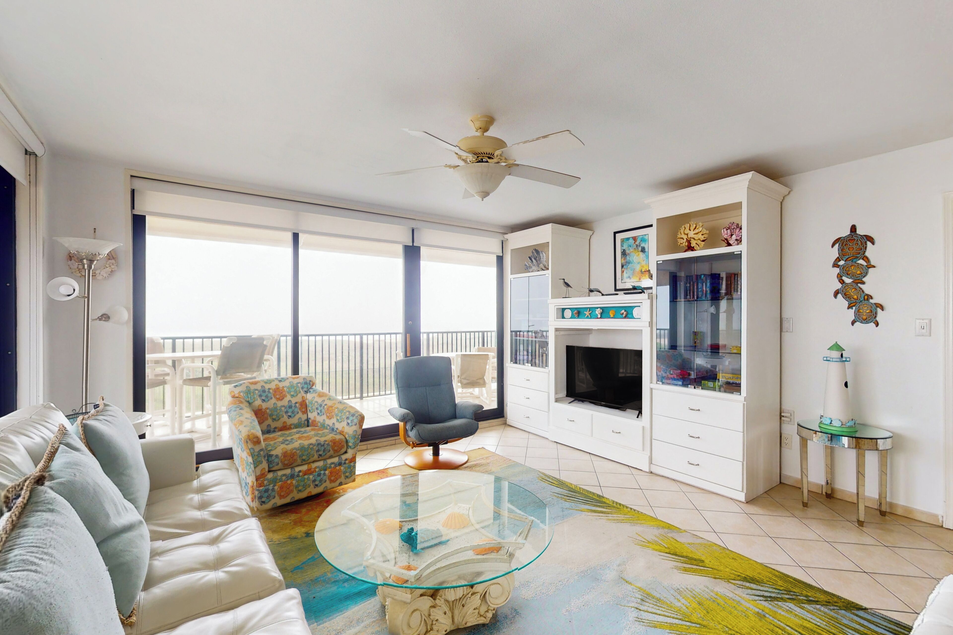 A living room with a sofa, armchair, glass coffee table, and a ceiling fan.