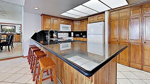Eine moderne Küche mit Holzausstattung, einer großen Kochinsel mit Sitzgelegenheiten, einer Mikrowelle und einem Kühlschrank.