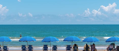 A beach with multiple blue umbrellas and beach chairs.