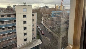 A view of a multi-story building with a flat roof and a small attached structure with a sloped roof. There is a construction crane in the distance, indicating ongoing development. - Modern Bright Top-floor Flat (London)