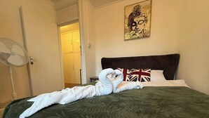 A bed with a dark green cover, a white towel, and a British flag pillow. - Modern Bright Top-floor Flat (London)