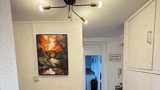 A hallway with a ceiling light fixture, a radiator, a framed picture, and a sign that says "THIS IS OUR HAPPY PLACE." - Modern Bright Top-floor Flat (London)