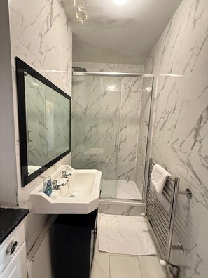 A modern bathroom with a glass-enclosed shower, a white sink with a mirror, and a towel rack. - Modern Bright Top-floor Flat (London)